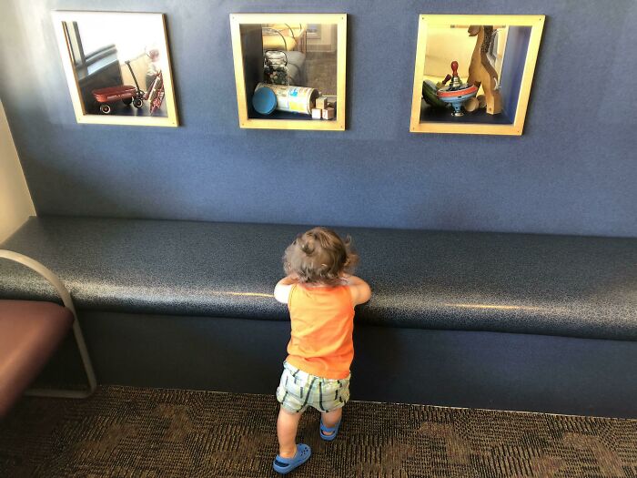 A child in an orange shirt stands before unfortunate public interior designs with awkward wall shadowboxes.