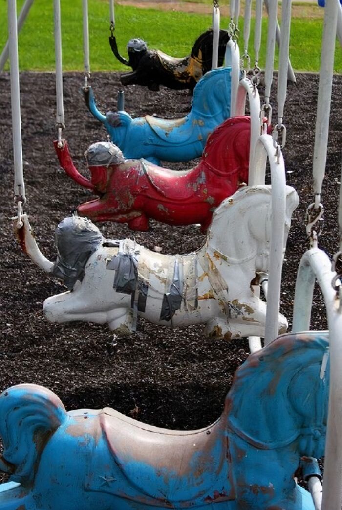 Worn-out carousel horses in a playground, showcasing a Gen X nostalgic vibe with weathered paint and duct tape repairs.