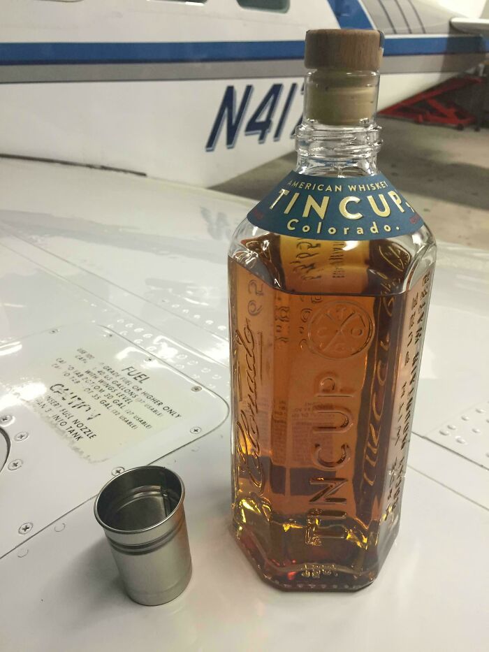 Tin Cup whiskey bottle with metallic cup, showcasing cool product surprise on an airplane wing.