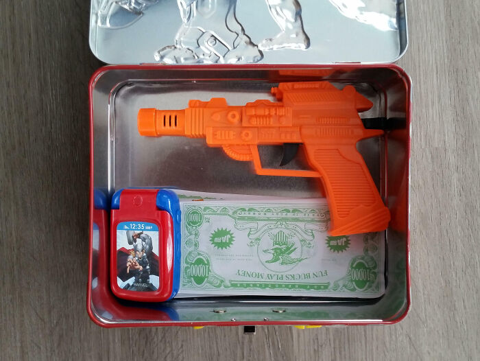 Toy set with orange water gun, play money, and toy phone in a metal box. Hilarious-Kids play essentials.