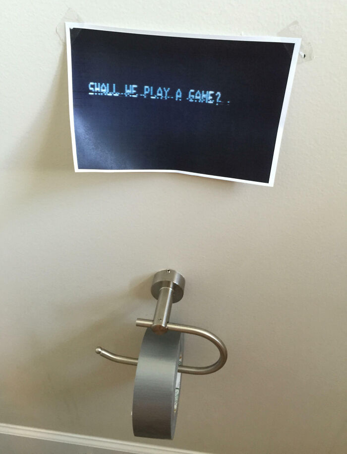 Sign with "Shall we play a game?" above an empty toilet paper holder, showcasing hilarious kids' humor.