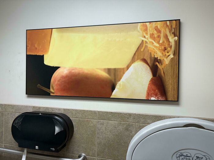 Unfortunate public interior design: large kitchen-themed artwork in a restroom above a toilet paper dispenser.