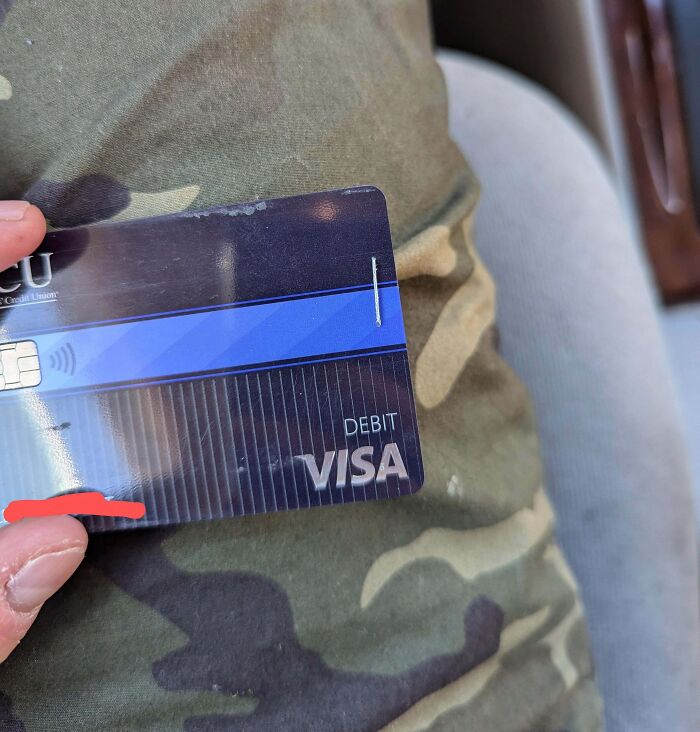 A Visa debit card held in front of camo pants, representing infuriating local pharmacies issues with credit cards.