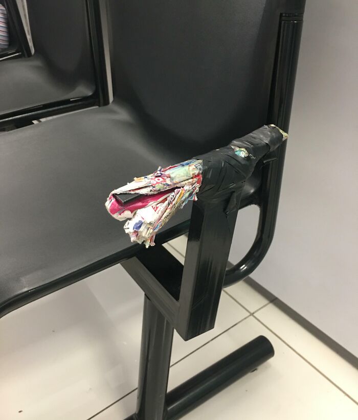 Damaged pharmacy chair with a makeshift armrest made of taped magazines.