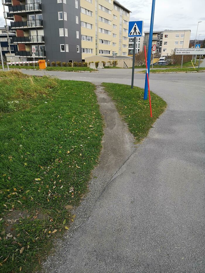 Worn-down path in grass showing the passage of time in an urban setting with buildings and pedestrian signs.