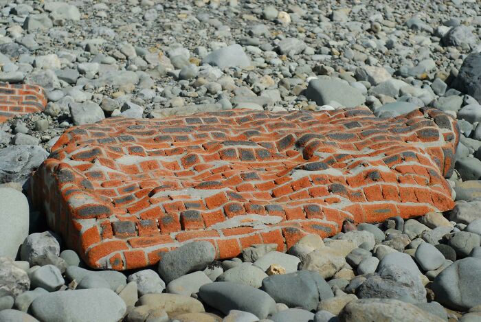 Worn-down brick structure on a rocky beach, illustrating the effects of time on man-made objects.