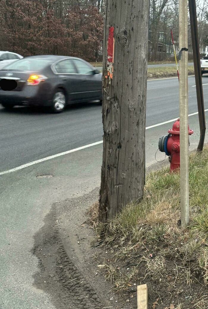 Worn-down wooden utility pole by the roadside with a passing car and a fire hydrant nearby, illustrating time's impact.