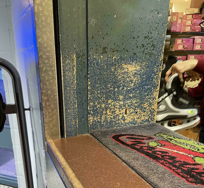 Worn-down counter corner in a store with visible paint chipping and customer holding a shoe in the background.