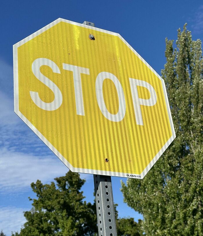 Worn-down yellow stop sign showing signs of aging under a clear blue sky.