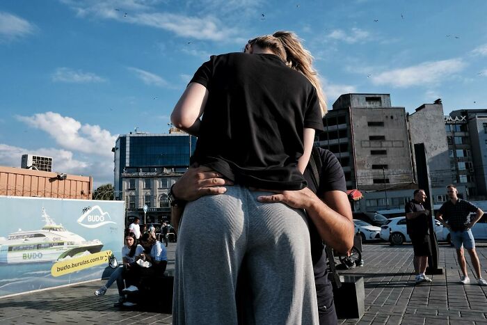 Street photographer captures humorous optical illusion of two people seemingly merged in a busy urban scene.