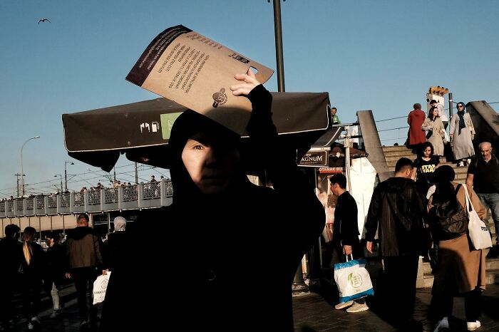 Street photographer captures a funny moment as a person holds a large paper, casting a shadow on their face.