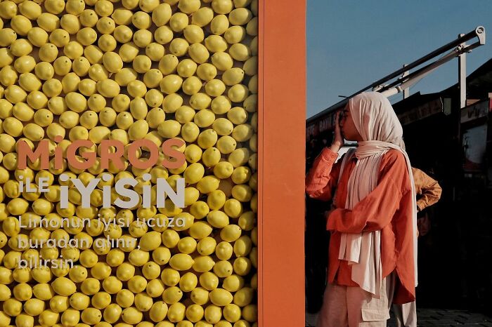 Street photographer captures a person standing beside a wall filled with lemons, with bold text on the display.