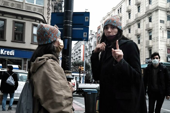 Street photographer captures funny moment between two people in patterned hats on a busy city intersection.