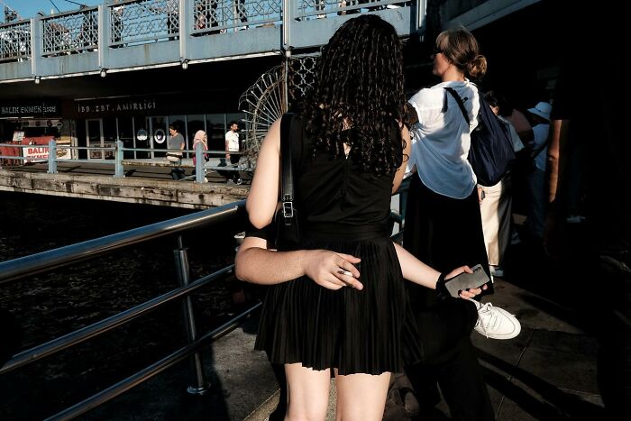 Street photographer captures a funny optical illusion with a woman on a bridge holding a phone and cigarette.