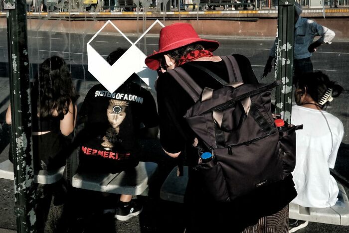 Street photographer captures a humorous scene with a person wearing a red hat and backpack near a bus stop, showcasing accidental hilarity.