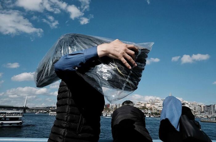 Street photography captures a person carrying a large plastic bag with a cityscape and river in the background.