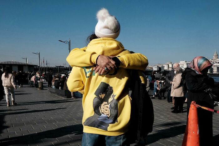 Street photographer captures a funny embrace between two people with a comic-style print on a yellow hoodie.