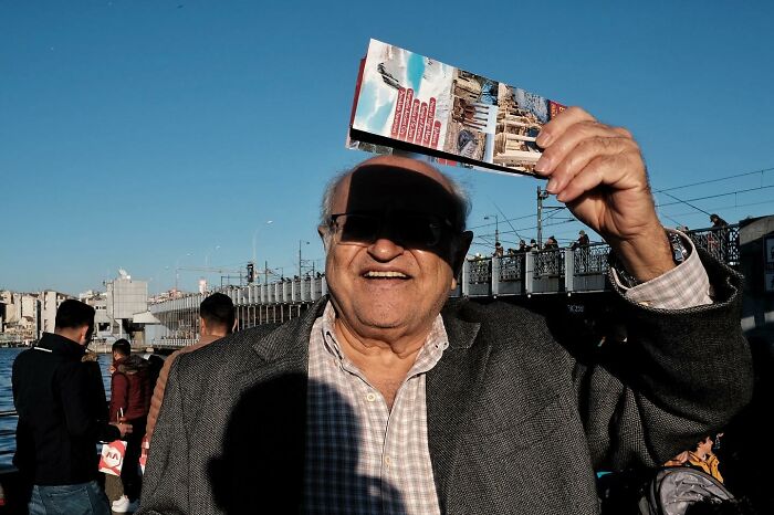 Man holding a brochure with a shadow cast on his face, captured by a street photographer.