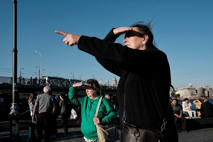 Street photographer captures a humorous moment with two people pointing and shielding their eyes from the sun.