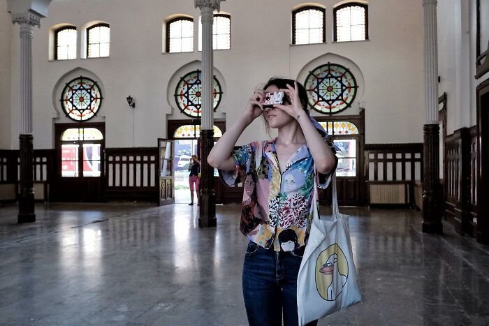 Street photographer captures woman with a camera in a colorful shirt inside a historic building with stained glass windows.