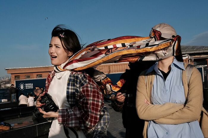 Street photographer captures hilarious moment with a scarf blowing into someone's face.