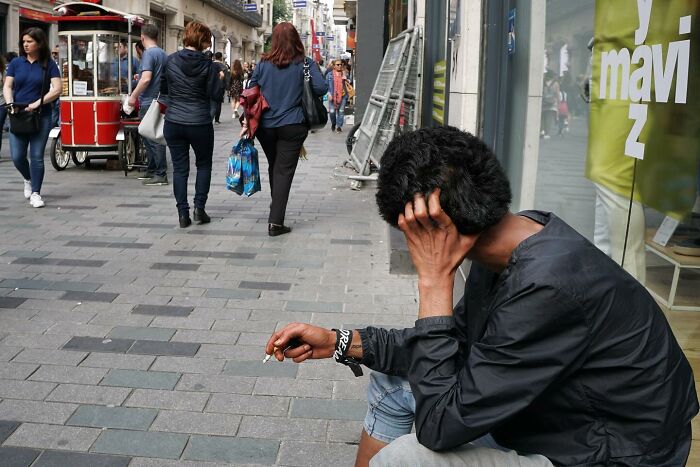 Street photographer captures candid moment of a person sitting on a busy sidewalk, surrounded by pedestrians.