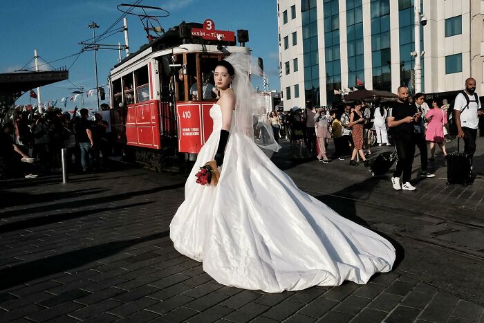 Street photographer captures bride in white dress posing by a tram, surrounded by a bustling crowd.