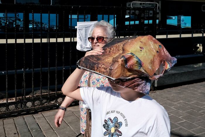 Street photographer captures a hilarious accidental scene of a child shielding face with a colorful bag in the sun.