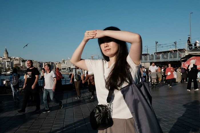 Street photographer captures woman shielding her eyes from the sun amidst a bustling crowd.