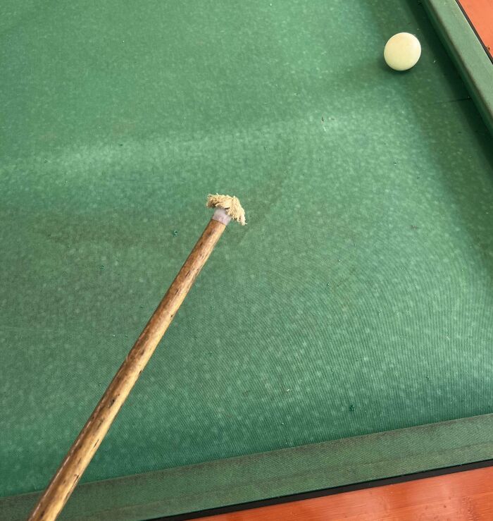 Billiard cue with worn-down tip on a green table, illustrating the effects of time.