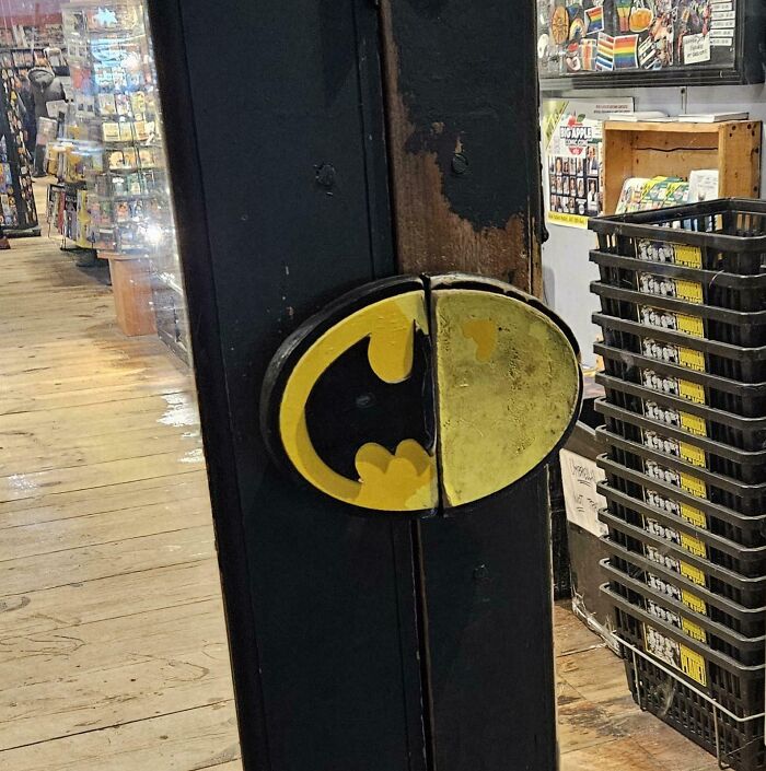 Worn-down Batman logo door handle inside a comic book store, illustrating time's impact on objects.