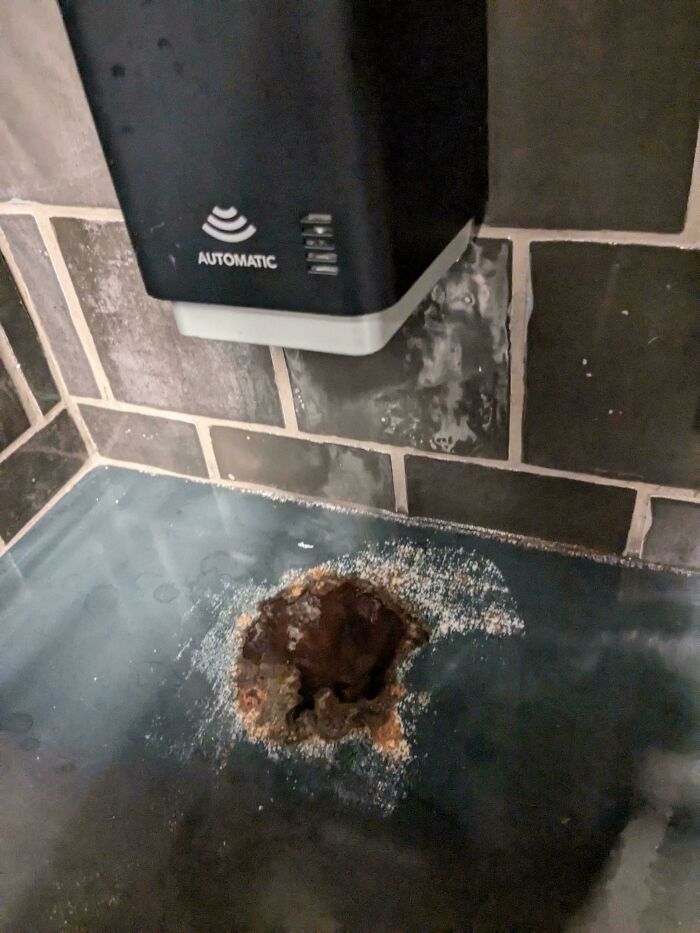 "Worn-down countertop under an automatic soap dispenser, showing significant wear from time and use."