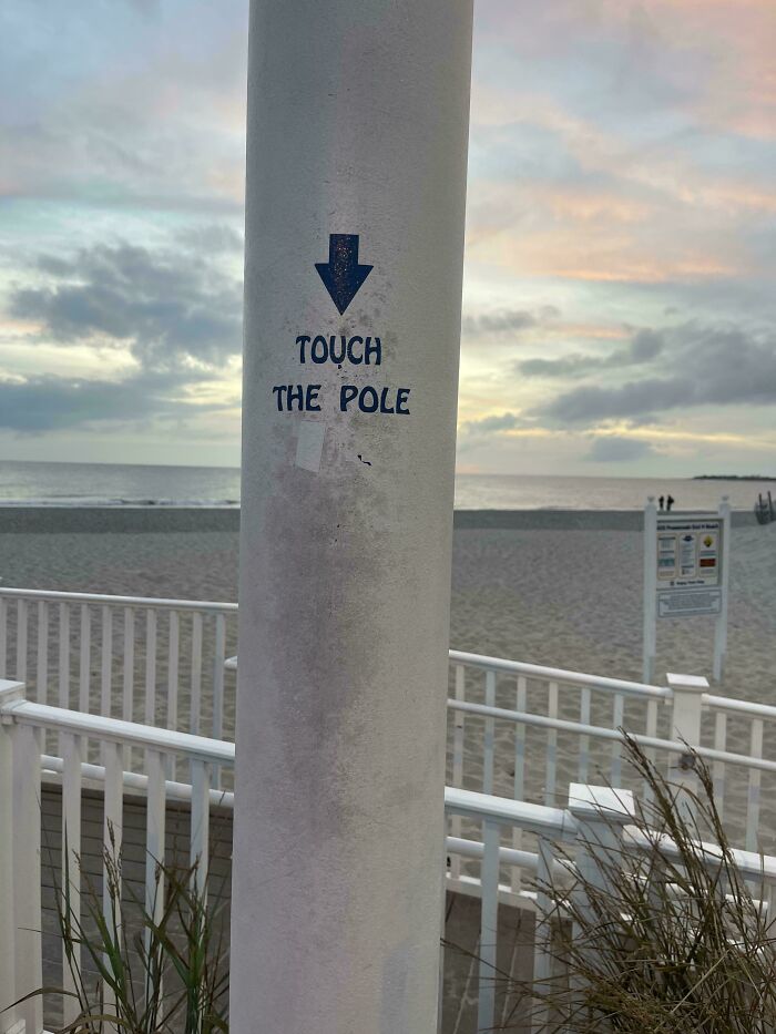 Worn-down pole at the beach with "Touch the Pole" sign, illustrating the effects of time.