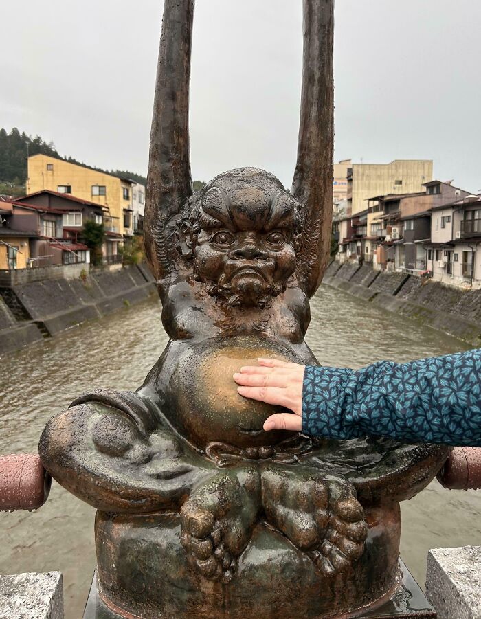 Hand touching a worn-down statue with a shiny belly, illustrating how time affects objects.