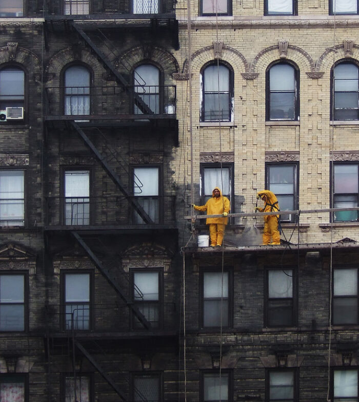 Workers in yellow suits cleaning a worn-down building facade, illustrating effects of time.