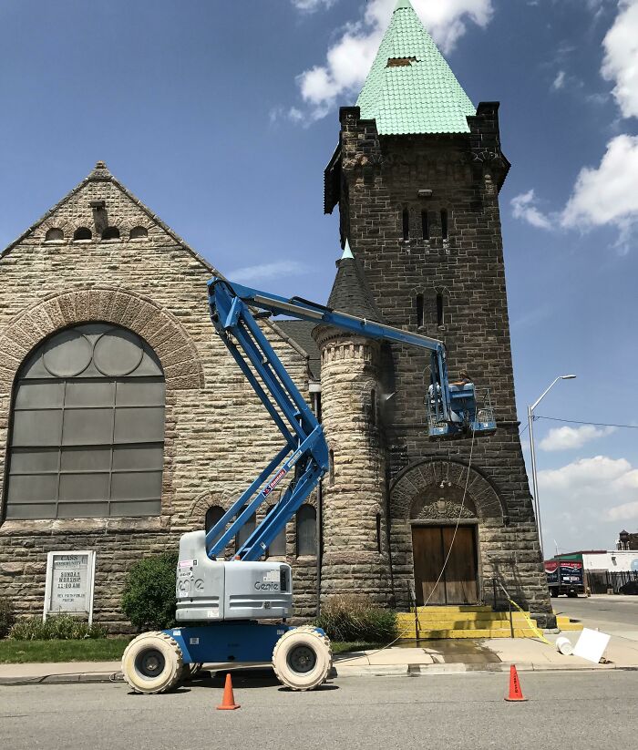 A worn-down brick church being repaired with a blue lift under a clear sky.