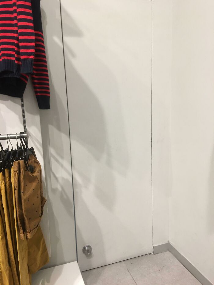 Unfortunate interior design showing a door behind clothing rack, making access challenging.