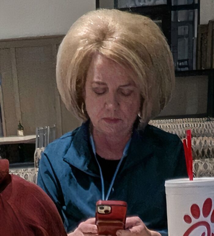 Woman with a voluminous blonde hairstyle, sitting indoors and focused on her phone, highlighting tragic hair accidents.