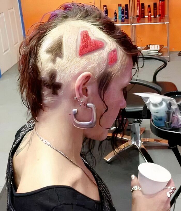 Person with shaved hair, showing card suit designs in colors, in a salon setting, highlighting a unique hair accident.