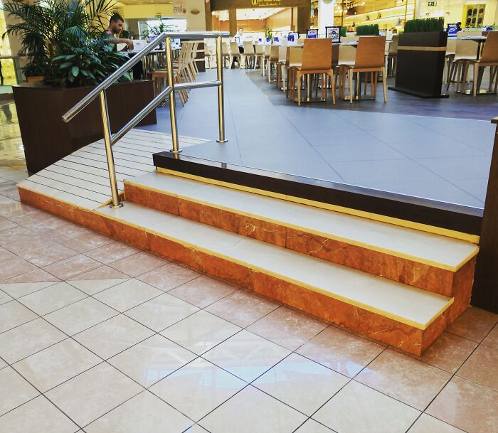 Unfortunate public interior design showing a ramp and stairs leading to a seating area in a mall.