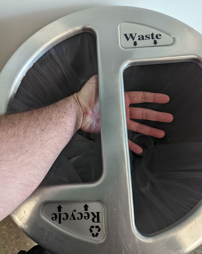 A hand stuck in an unfortunate public interior design of a circular waste and recycle bin lid.