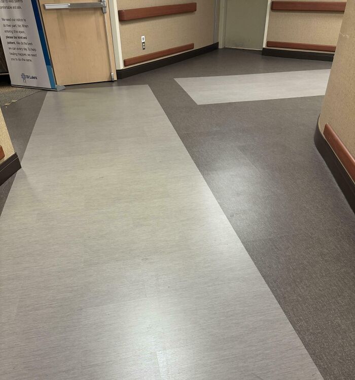 Unfortunate interior design featuring mismatched flooring patterns in a hallway with beige walls and a safety handrail.