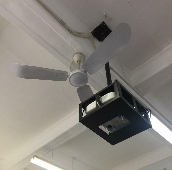 Ceiling fan awkwardly placed on top of a mounted projector, showcasing unfortunate interior design.