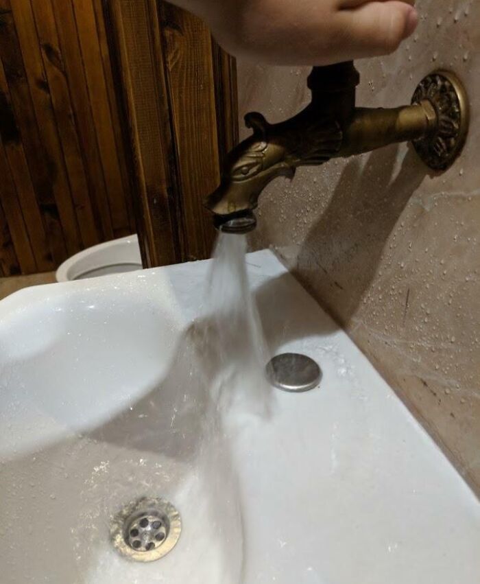 Unfortunate interior design with misaligned faucet pouring water onto the bathroom floor.