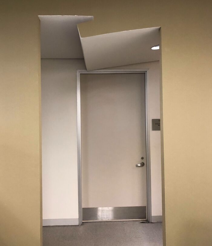 Unfortunate public interior design showing a door with a misaligned ceiling panel above it.