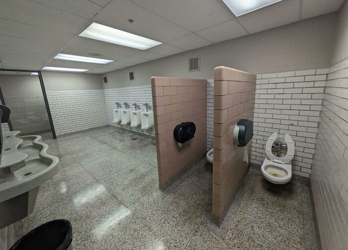 Public restroom with poor interior design: urinals and toilets lack privacy due to open partitions and awkward layout.