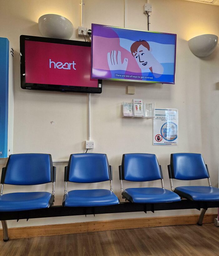 Unfortunate public interior design with mismatched screens and blue chairs in a waiting area.