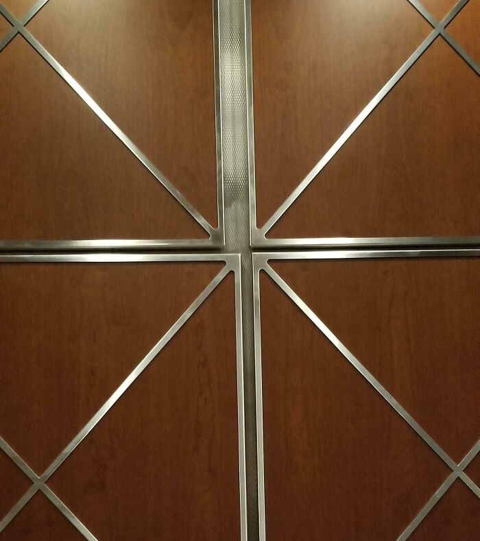 Unfortunate public interior design with awkwardly placed metal trim over wood panels, creating an uneven appearance.