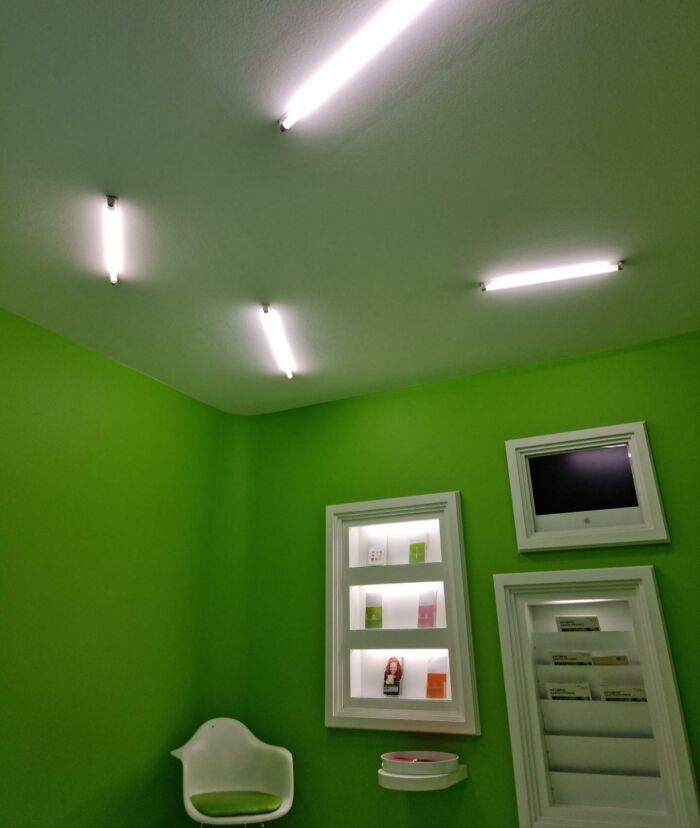 Fluorescent lights on a bright green wall with misaligned decor, showcasing unfortunate public interior designs.