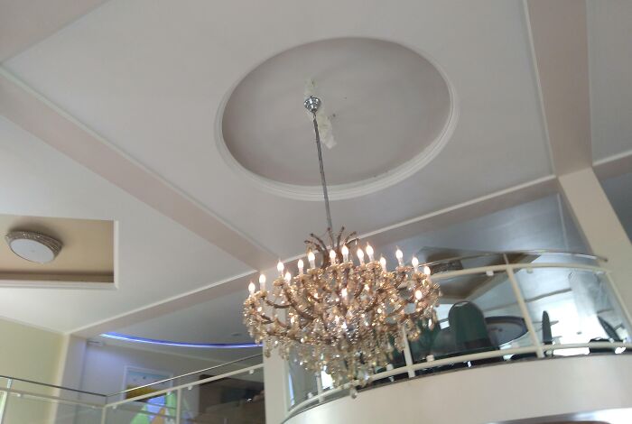 A lavish chandelier awkwardly positioned off-center from the ceiling medallion, showcasing unfortunate public interior design.